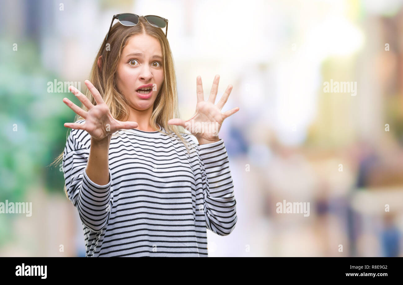 Young beautiful blonde woman wearing sunglasses over isolated background afraid and terrified with fear expression stop gesture with hands, shouting i Stock Photo