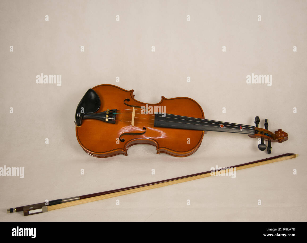 A brown violin with four strings and a violin bow on a white background Stock Photo