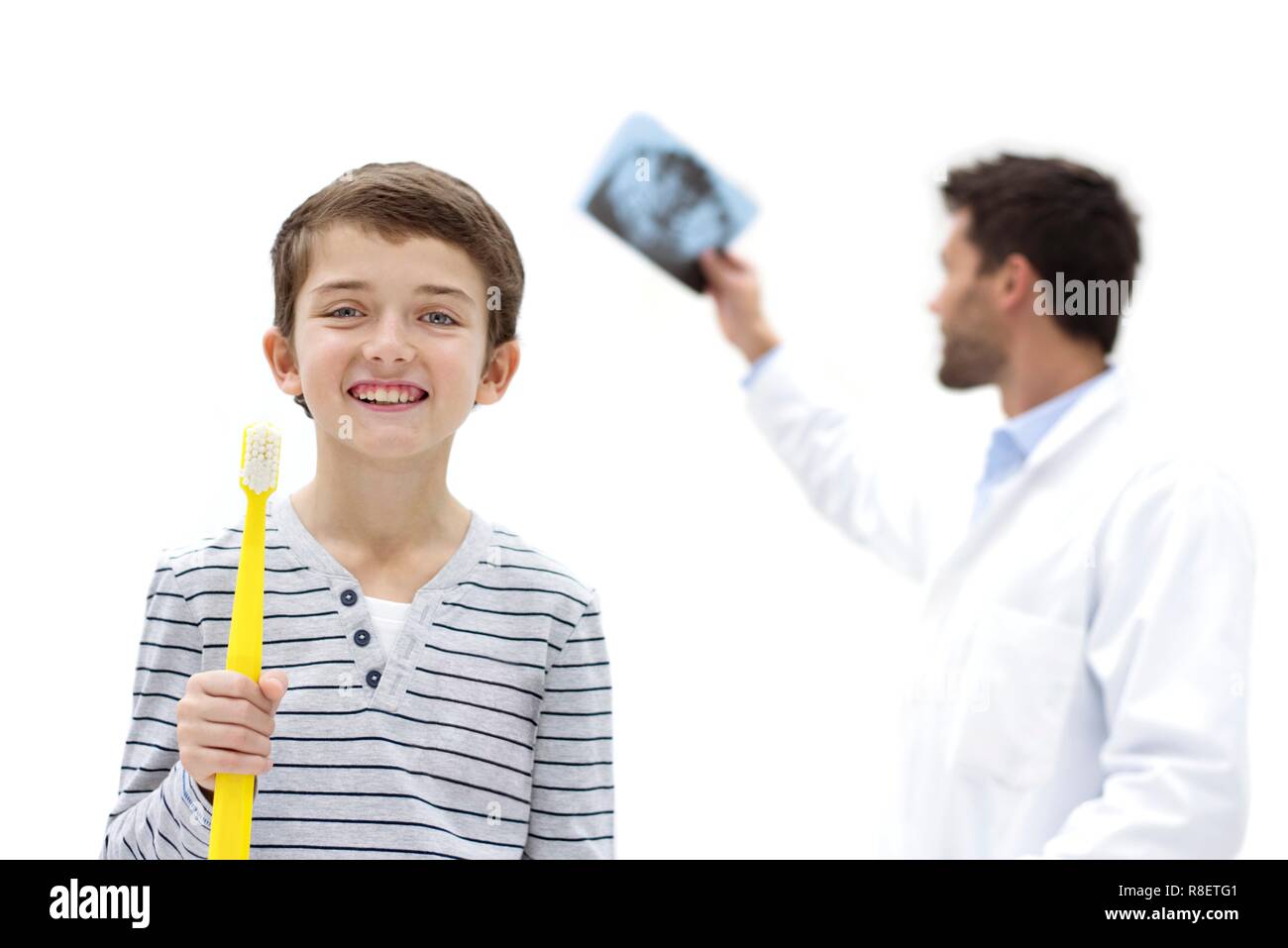 Boy holding over sized toothbrush in dental surgery, with doctor holding dental x-ray. Stock Photo