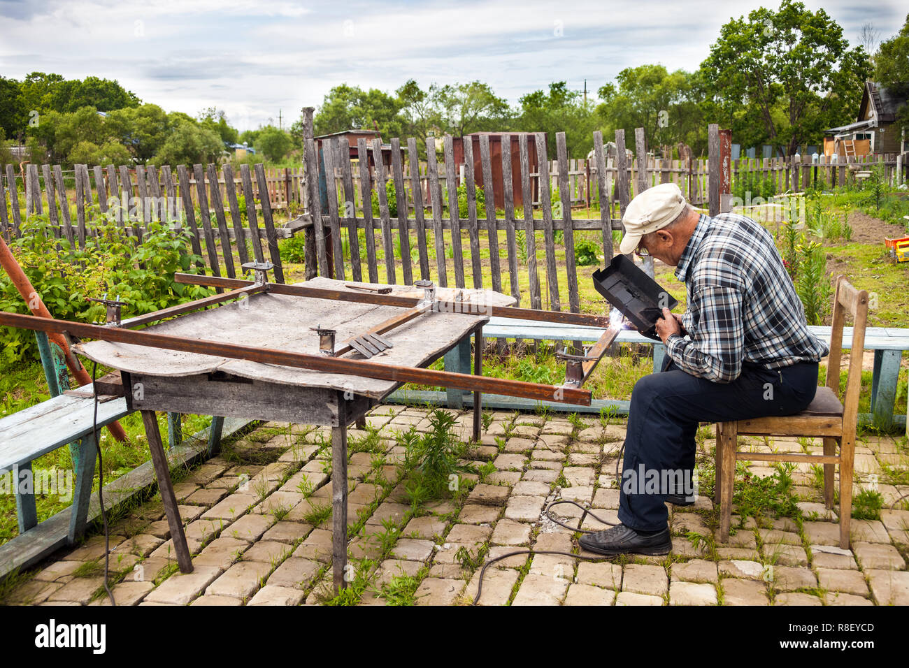 Aged man welding metal structure at his dacha Stock Photo