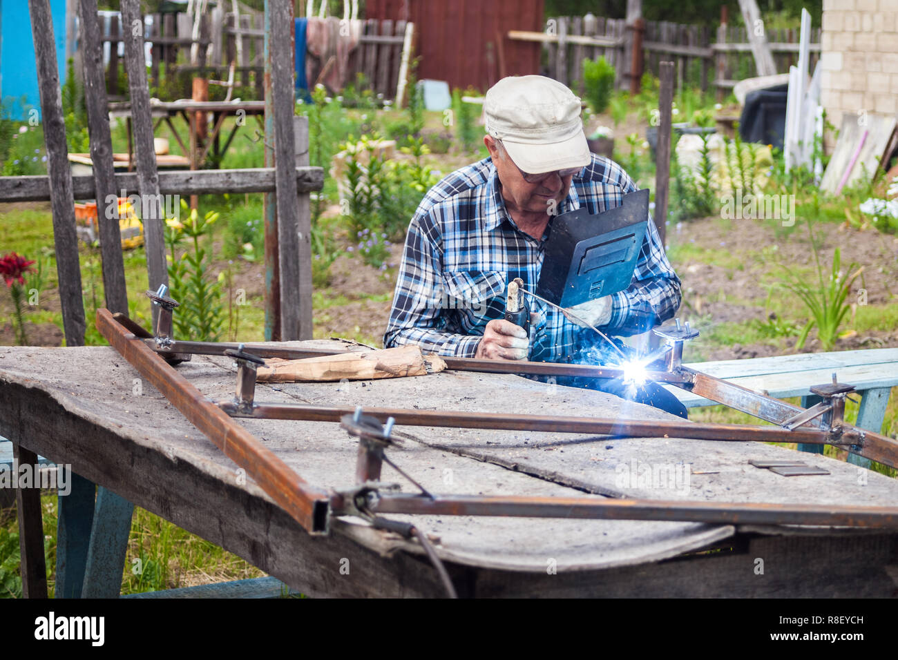 Elderly man welding metal structure at the garden Stock Photo