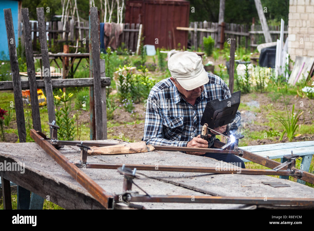 Elderly man welding metal construction at the garden Stock Photo