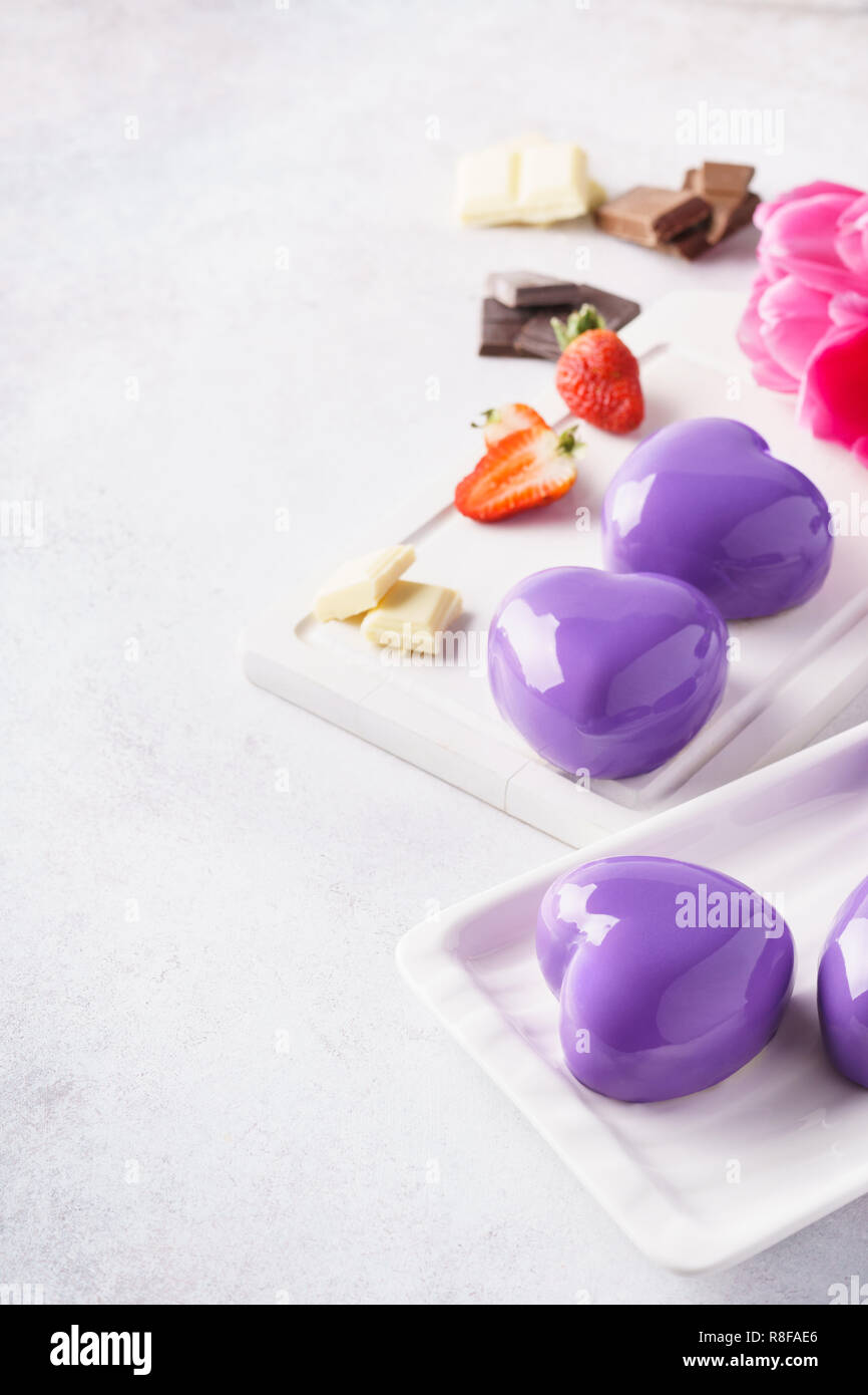 Mousse cakes with violet or purple mirror glaze, berries and chocolate. Stock Photo
