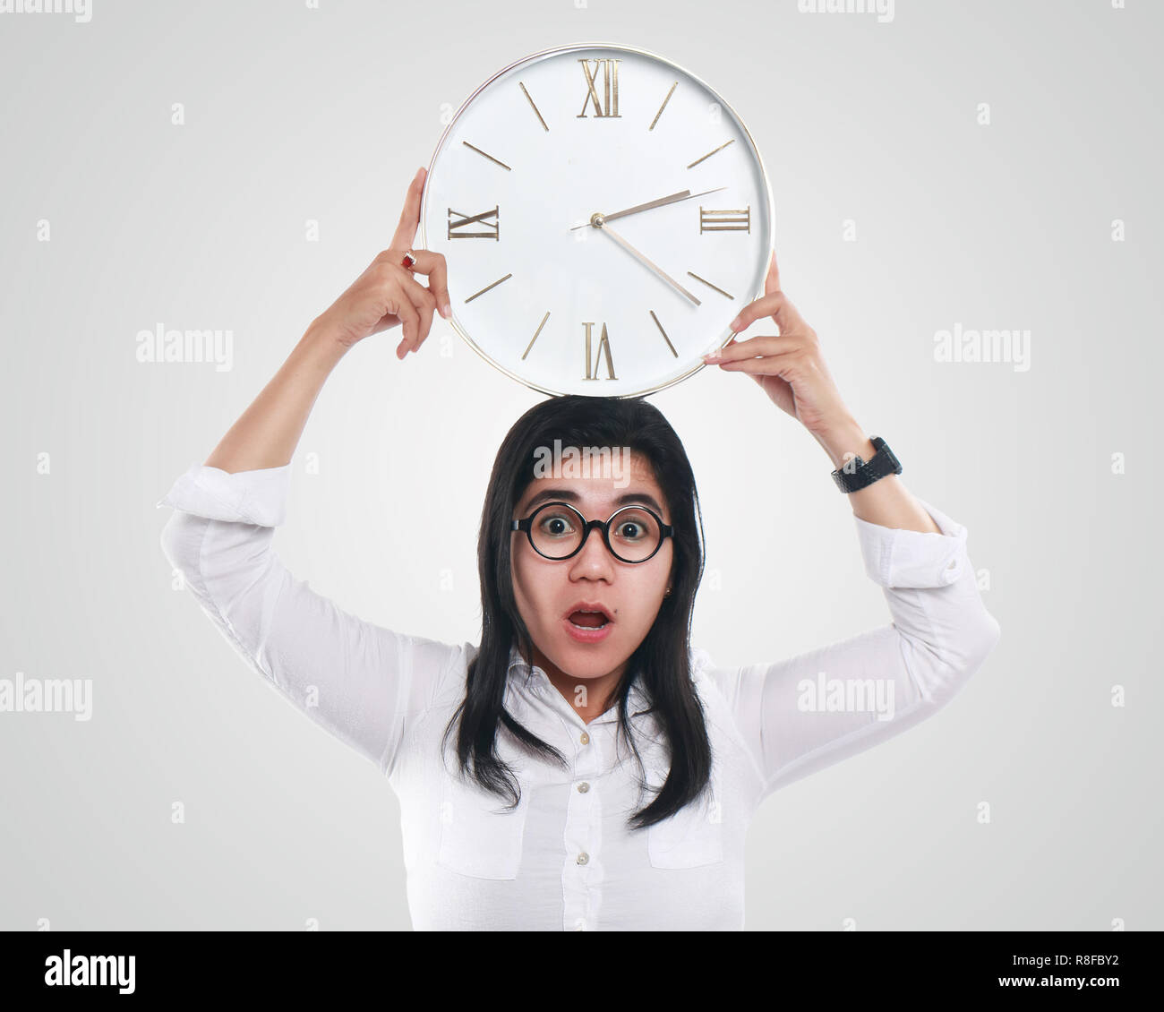 Photo image portrait of a beautiful young Asian businesswoman looked shocked while looking time on clock, with both hands holding the clock, half body Stock Photo