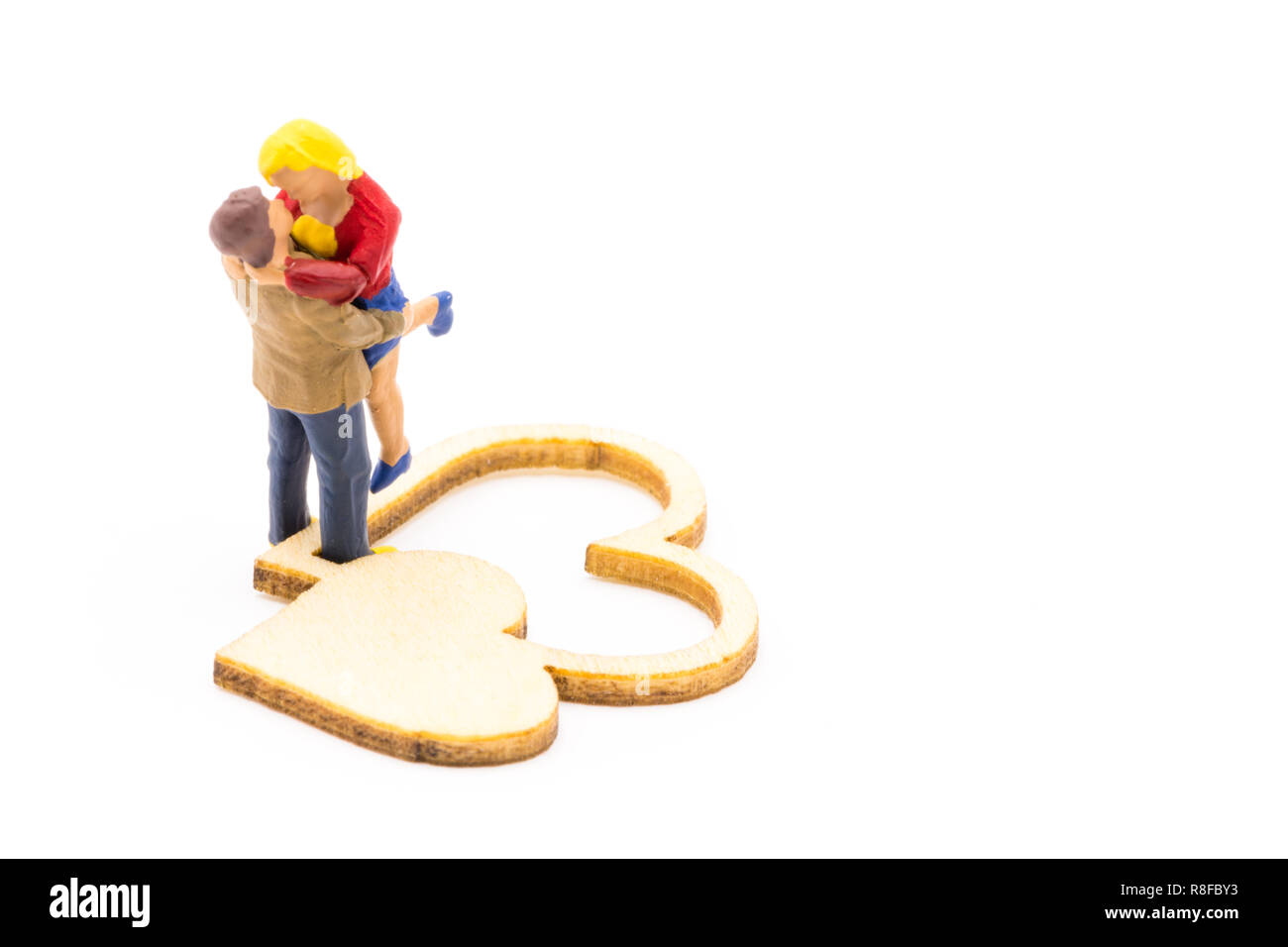 Miniature figures as in love hugging couple next to wooden hearts sign, isolated on white background Stock Photo