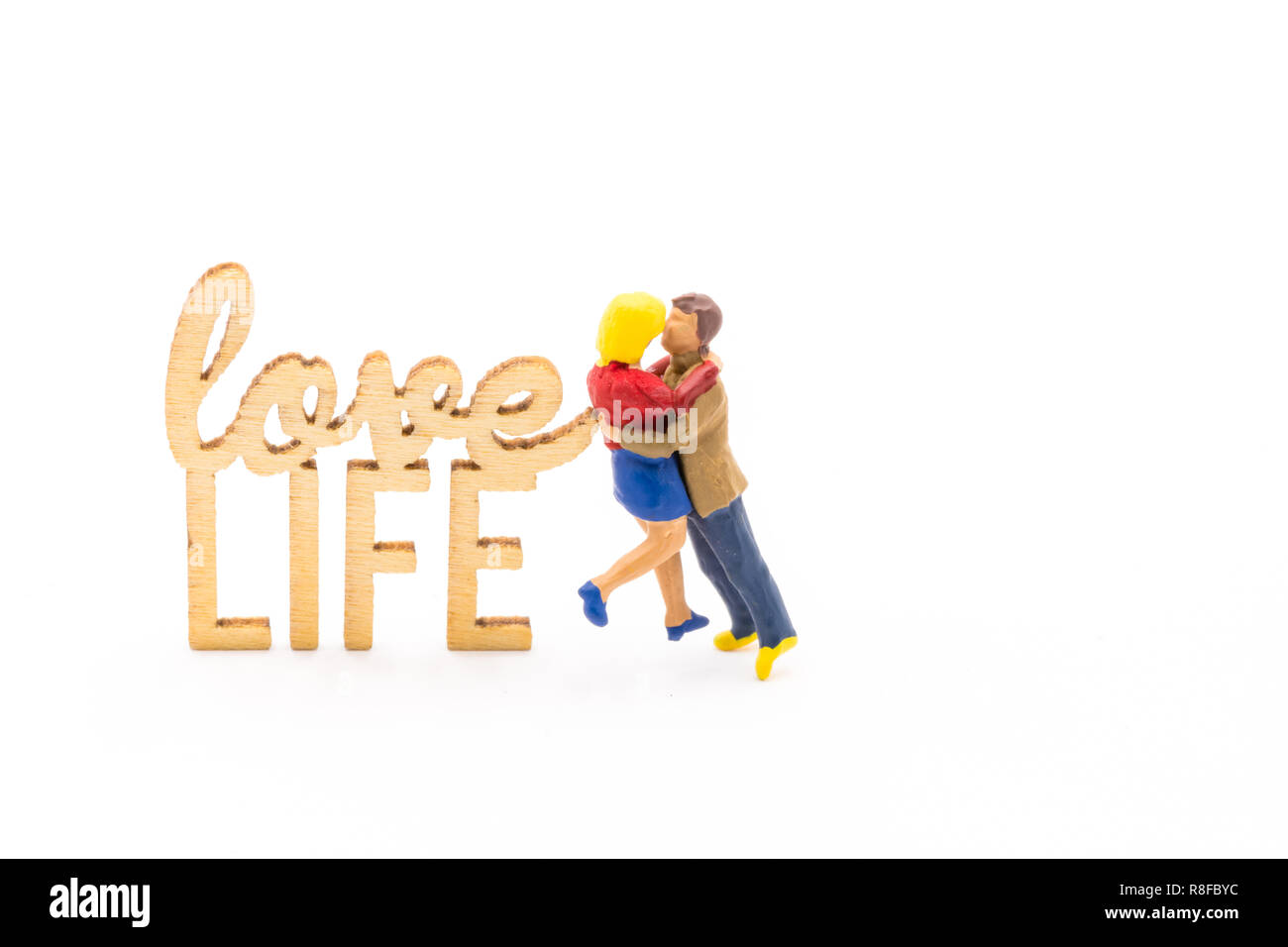 Miniature figures as in love hugging couple next to wooden sign with text Love Life, isolated on white background Stock Photo