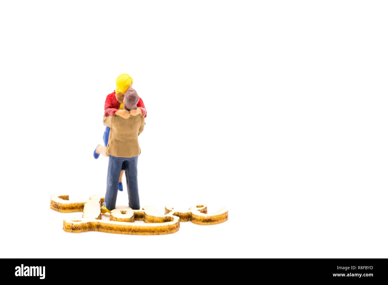 Miniature figures as in love hugging couple next to wooden sign with text Love, isolated on white background Stock Photo