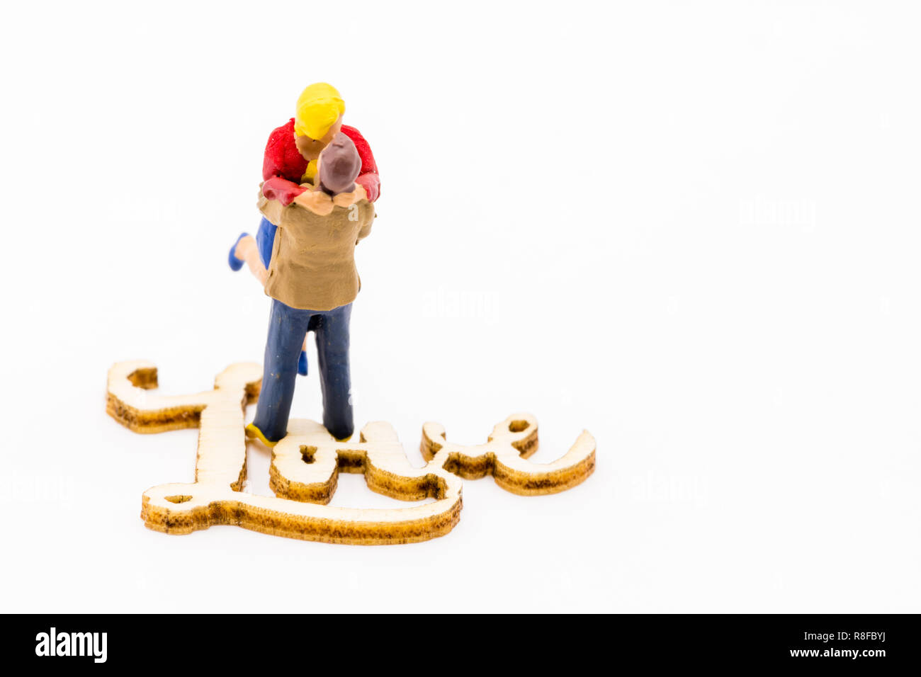 Miniature figures as in love hugging couple next to wooden sign with text Love, isolated on white background Stock Photo