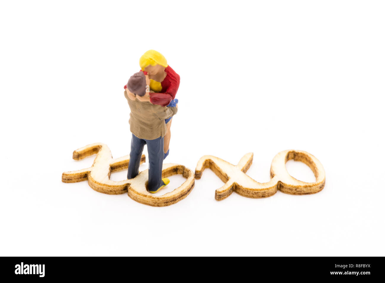 Miniature figures as in love hugging couple next to wooden sign with text XOXO, isolated on white background Stock Photo