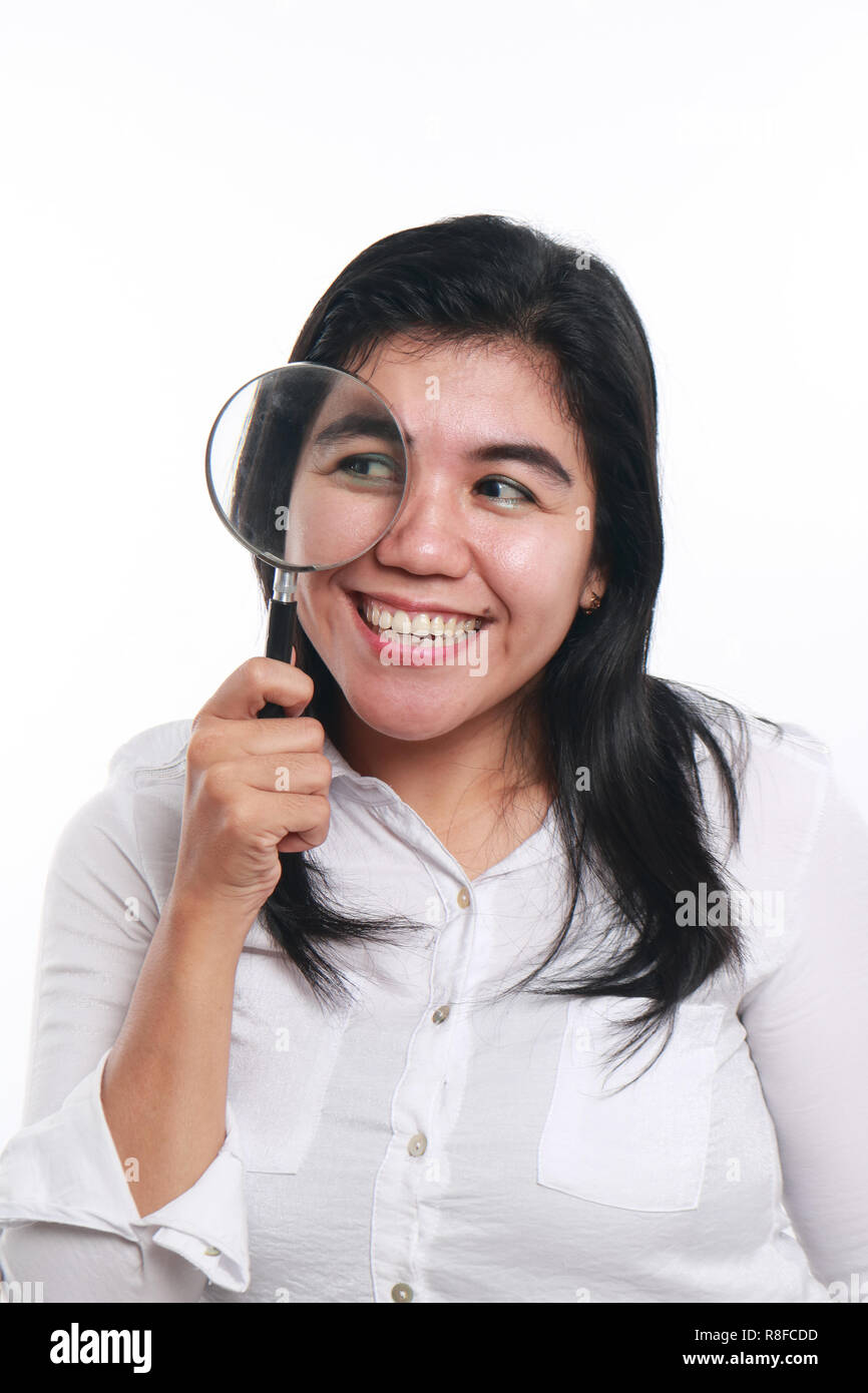 Photo image portrait of a beautiful cute young Asian woman looked very happy and smiling to find something while looking into magnifying glass Stock Photo