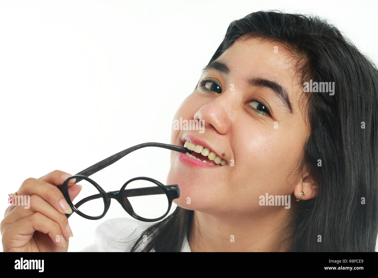 Photo image portrait of a beautiful cute young Asian woman with mole looked very happy smiling, biting her eyeglasses, close up portrait over white Stock Photo