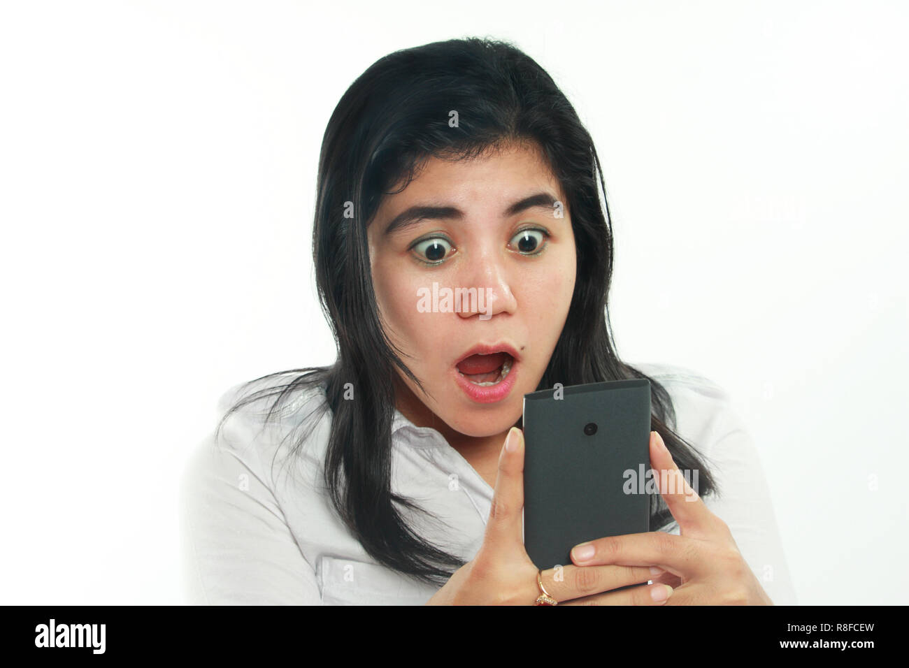 Photo image portrait of a cute young Asian woman with mole looked shocked looking her smart phone. Holding phone with both hands while reading message Stock Photo