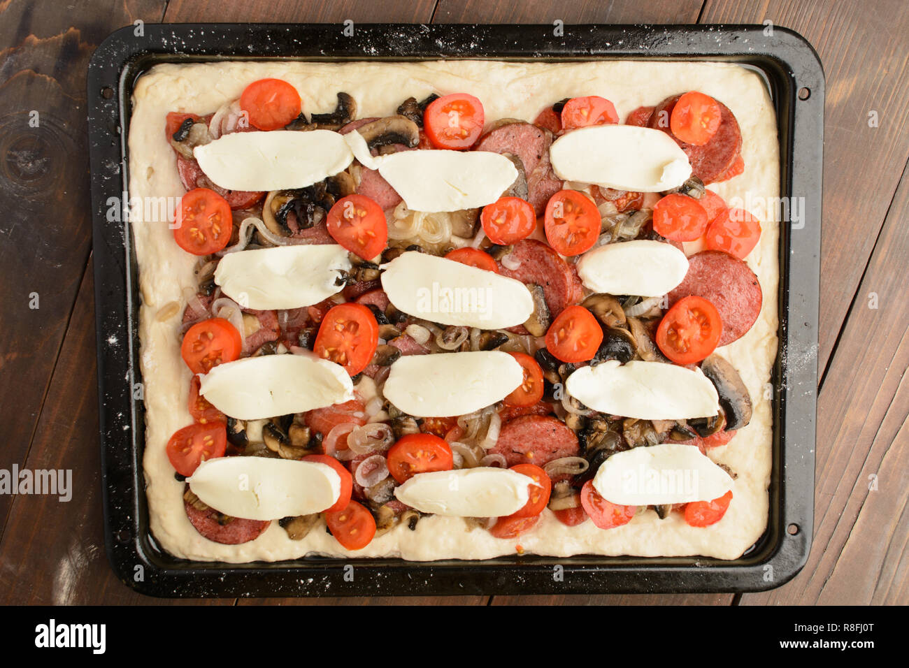 Unready homemade pizza with ingredients on baking pan over brown wooden background Stock Photo