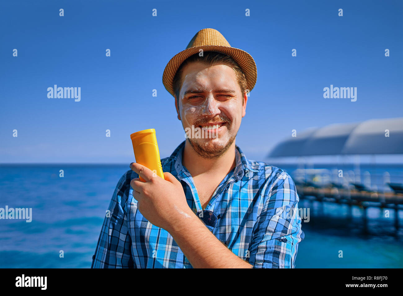 Guy put sun cream on the face. Man is on vacation, and he smeared with sunblock, and holds it in his hand. Stock Photo