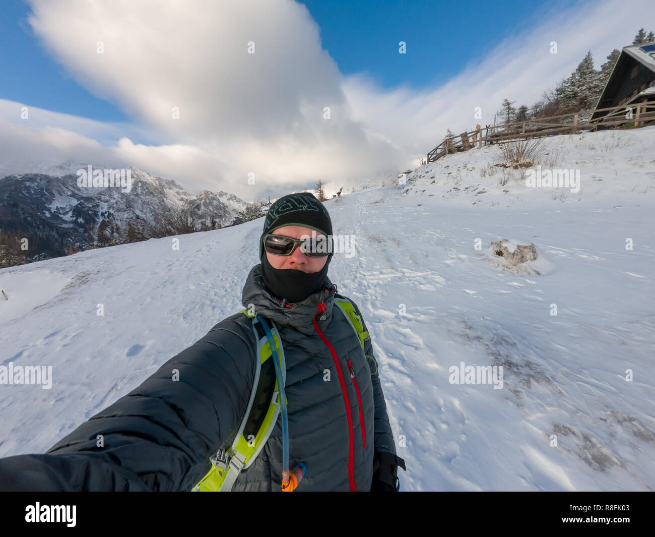 Mountaineer taking winter selfie while posing at snow covered hills. Active outdoor person enjoying cold weather. Stock Photo