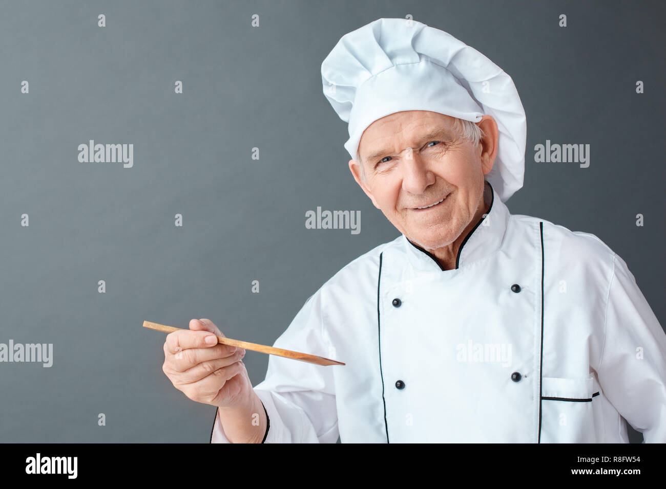 Senior chef studio standing isolated on gray holding spatula looking camera positive close-up Stock Photo