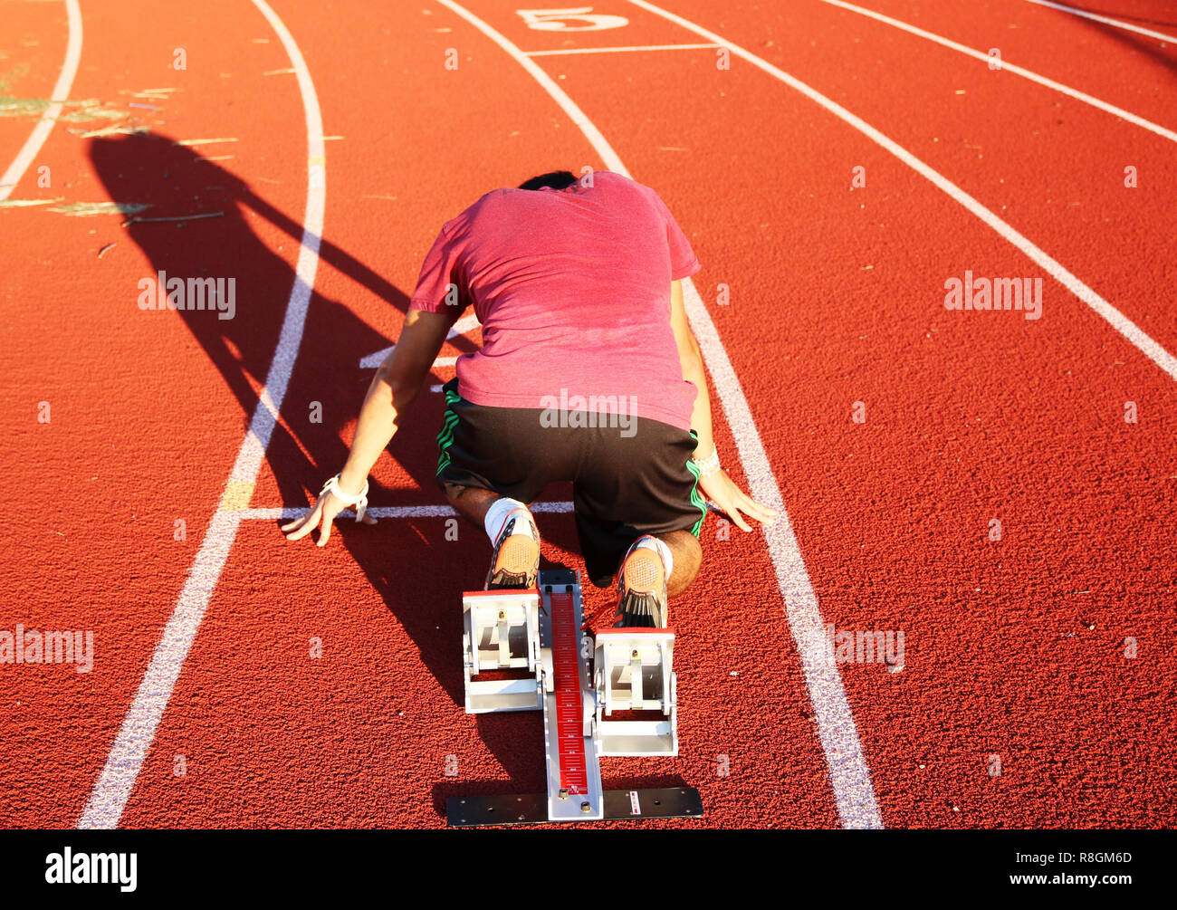 A track and field sprinter is in the starting blocks in the on your mark position at practice on a sunny summer day. Stock Photo