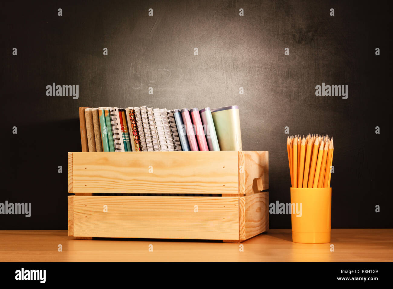 School notebooks in a row in a wooden box and pencils on a wooden school desk in front of a black chalkboard. Education concept - the desk in the audi Stock Photo