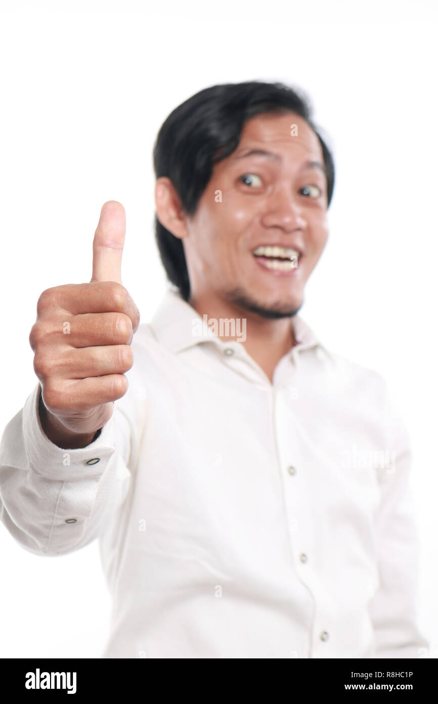 Photo image portrait of a cute funny young Asian man showing thumb up gesture with smiling face, close up portrait over white background, focus on han Stock Photo