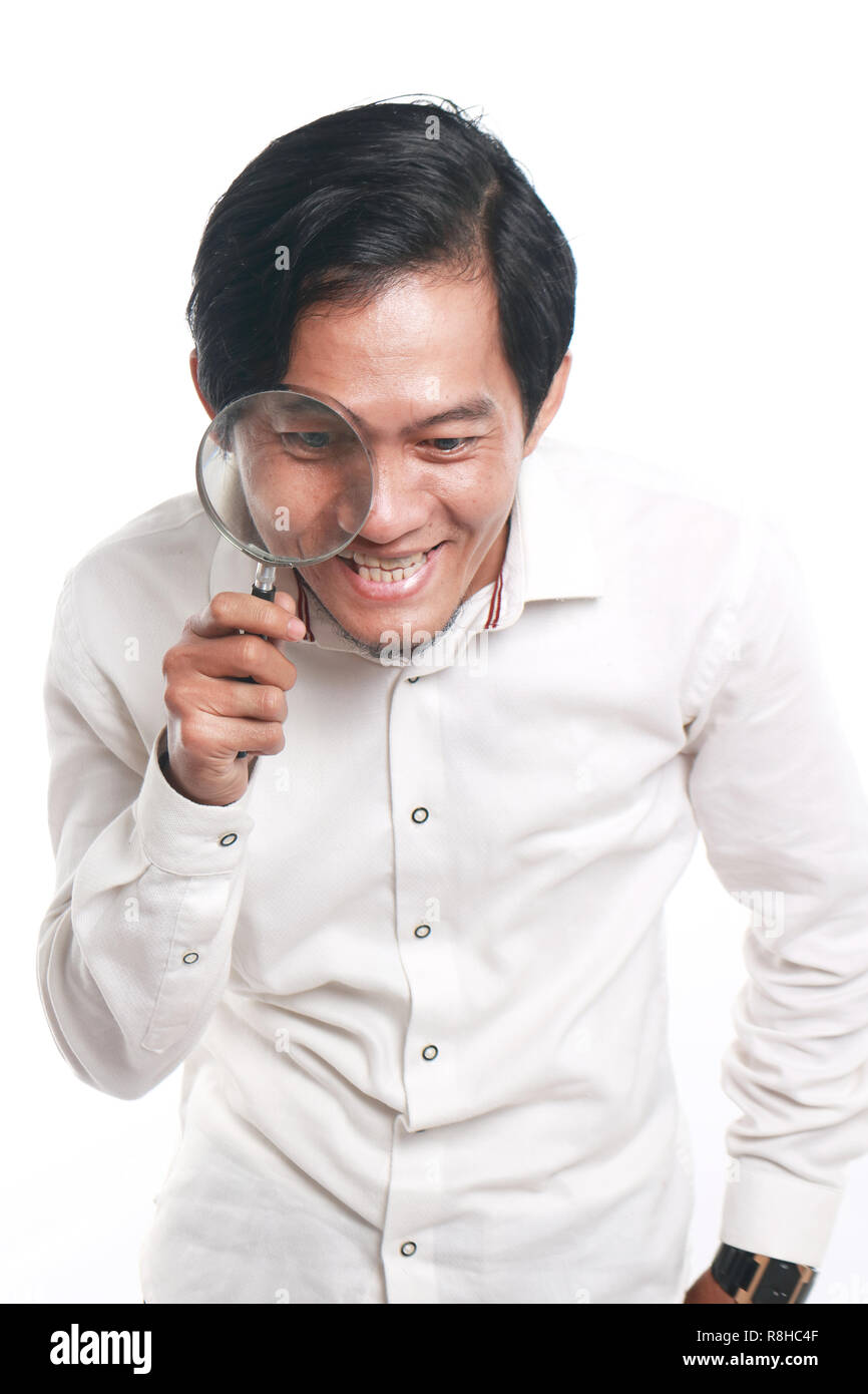 Photo image portrait of a funny young Asian businessman looked very happy and smiling to find something while looking into magnifying glass, close up  Stock Photo