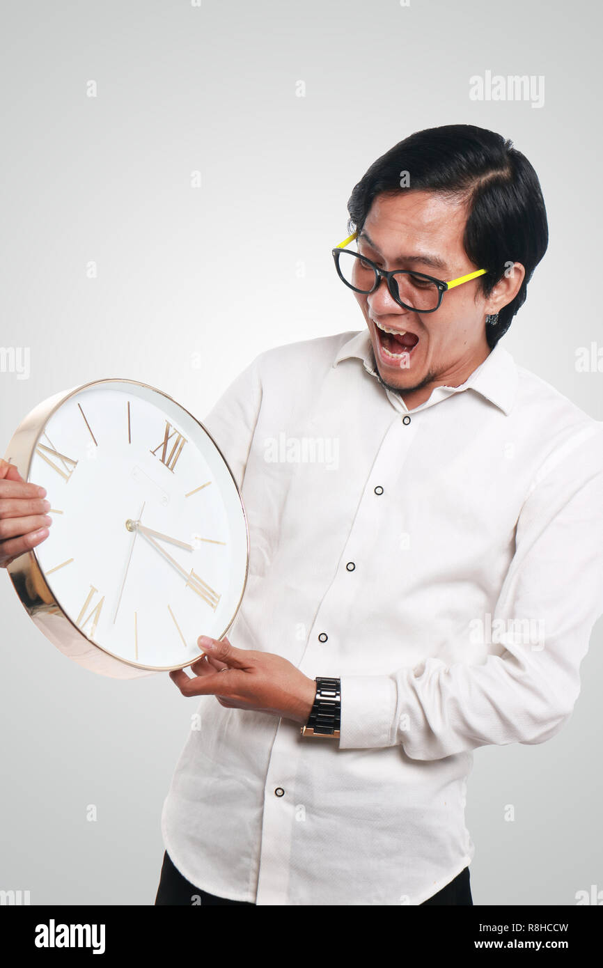 Photo image portrait of a funny young Asian businessman looked shocked while looking a clock that he hold, close up portrait, time or deadline concept Stock Photo
