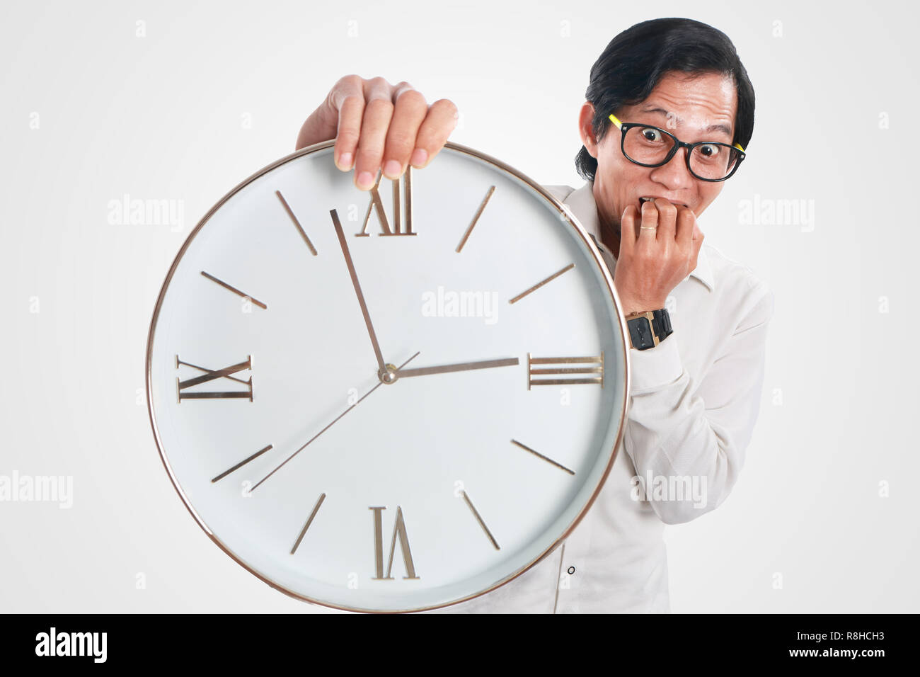 Photo image portrait of a funny young Asian businessman looked shocked and worried while showing a clock that he hold, close up portrait, time or dead Stock Photo