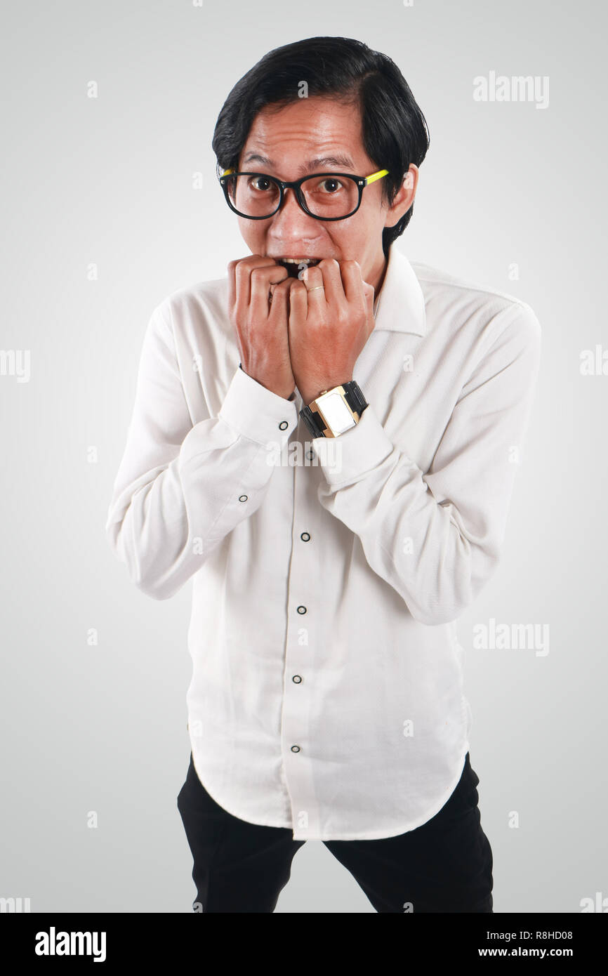 Photo image portrait of a funny young Asian businessman looked very scared and worried, half body close up portrait, biting nails gesture, above view Stock Photo