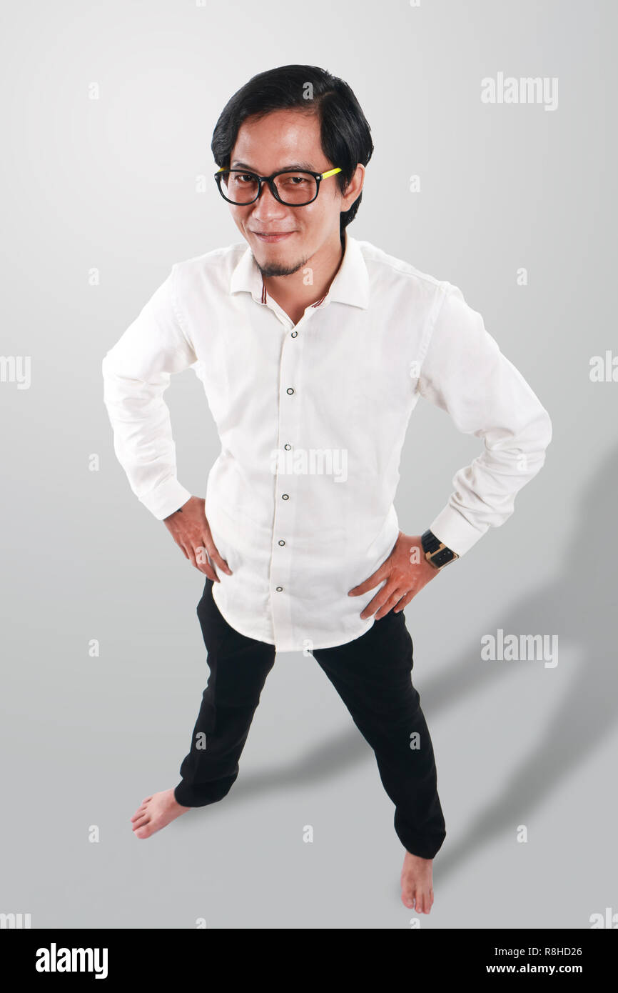 Photo image portrait of a funny young Asian man wearing glasses looked very proud and happy, smiling with both hands on his waist, full body portrait  Stock Photo