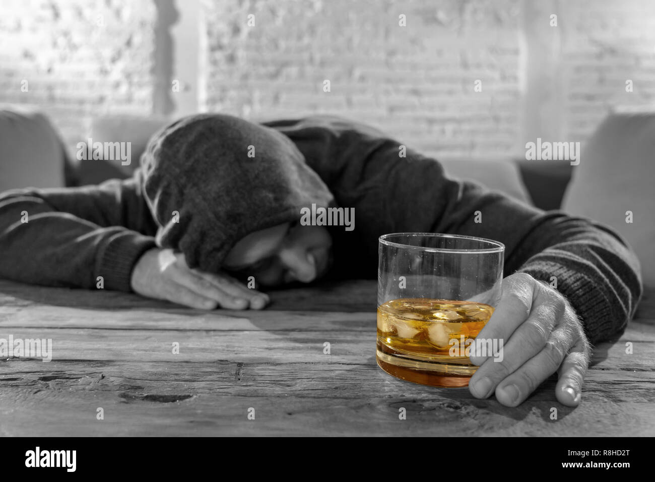 Drunk young man drinking alcohol at home felling lonely depressed and sick holding a glass of whiskey image in white and black and drink in color in A Stock Photo
