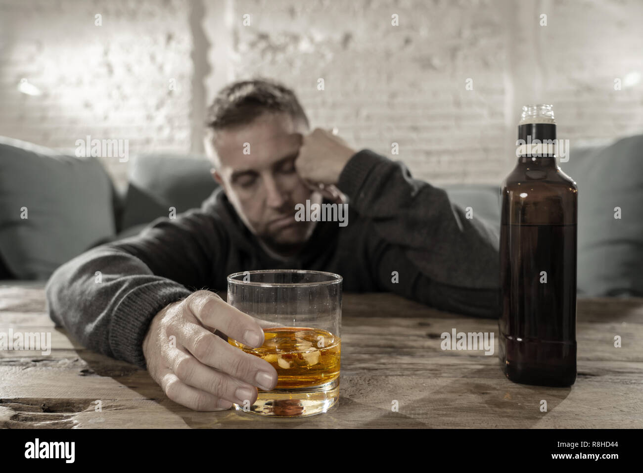 Drunk young man drinking alcohol at home felling lonely depressed and sick holding a glass of whiskey image in white and black and drink in color in A Stock Photo