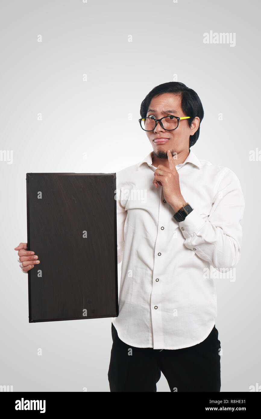 Photo image portrait of crazy Asian businessman or teacher or student holding blackboard with funny confused face and thinking gesture Stock Photo