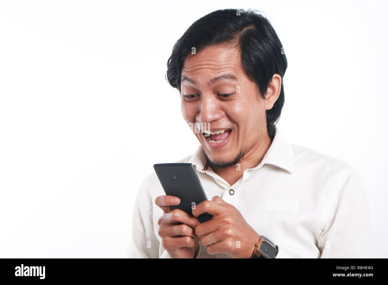 Photo image portrait of a funny young Asian man surprised and smiling while looking his smart phone. Holding phone with both hands while reading messa Stock Photo