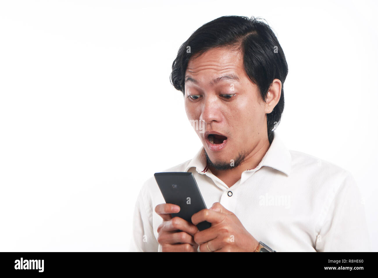 Photo image portrait of a funny young Asian man shocked while looking his smart phone. Holding phone with both hands while reading message on it, over Stock Photo