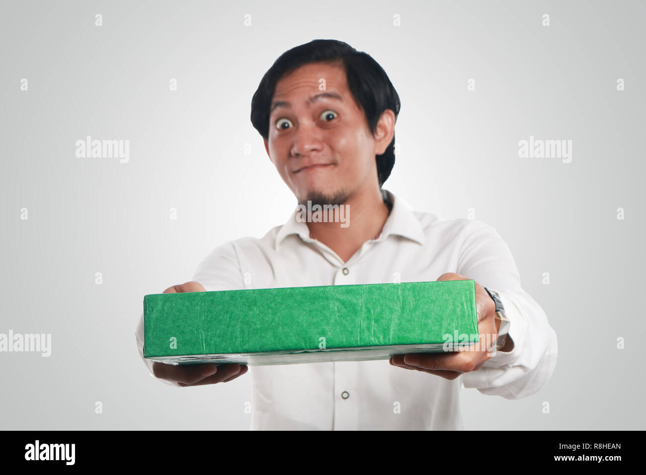 Photo image portrait of a funny young Asian man smiling happily with big eyes opened while giving green gift package box Stock Photo