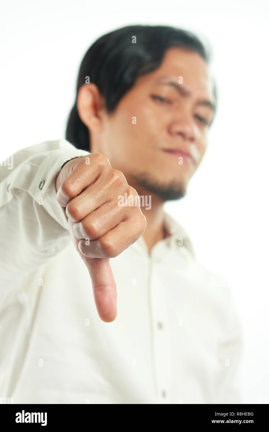 Photo image portrait of a funny young Asian man showing thumb down gesture with disappointed face, side view half body close up portrait over white, f Stock Photo