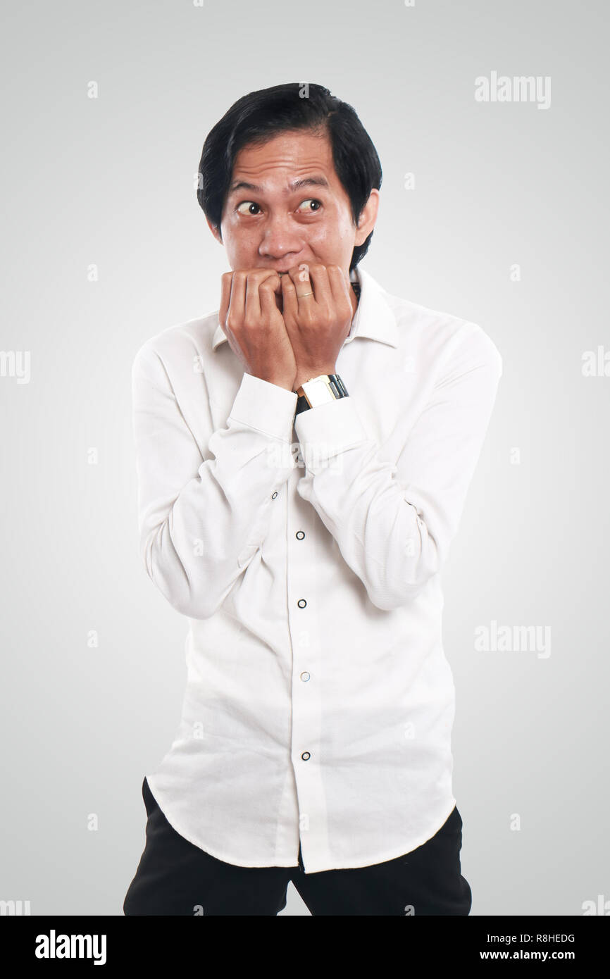 Photo image portrait of a funny young Asian businessman looked very scared and worried, half body close up portrait, biting nails gesture Stock Photo