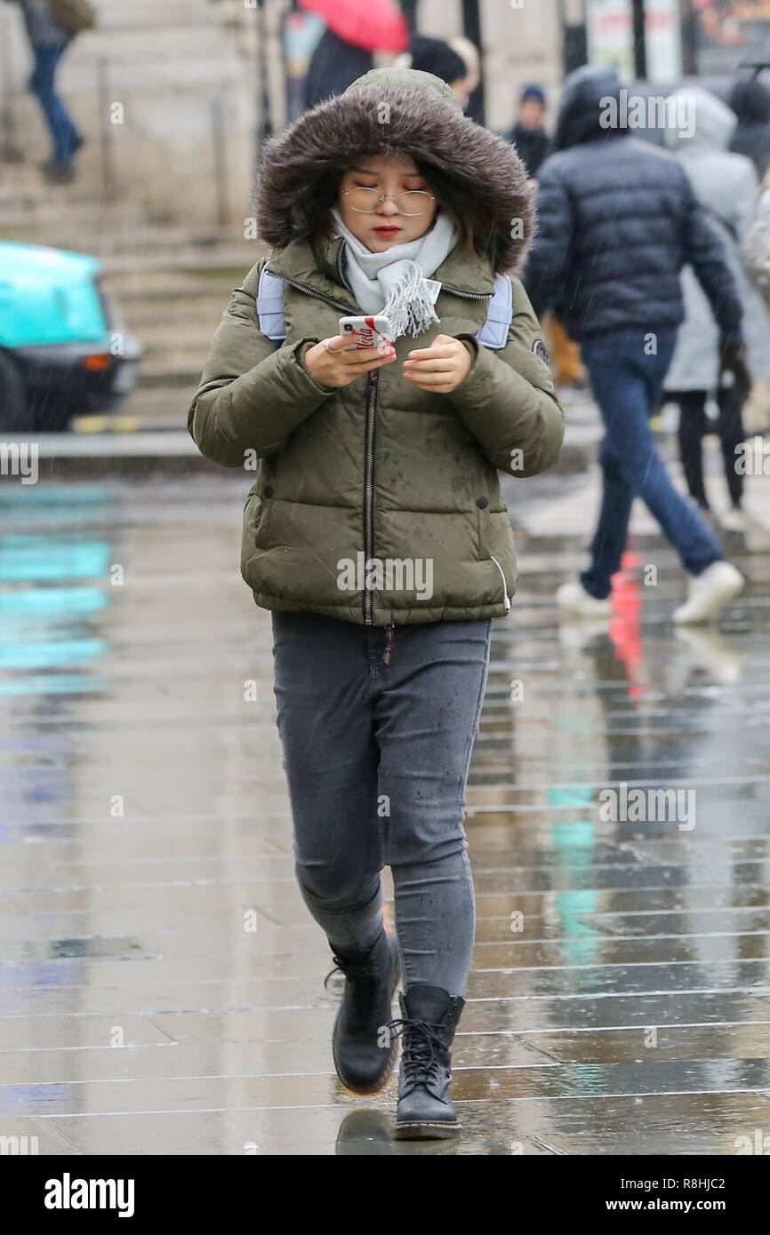 London, UK. 15th December 2018. A woman wrap-up warm wearing boots, scarf & winter  coat with hood up on a cold and wet day in London as snow has fallen in some