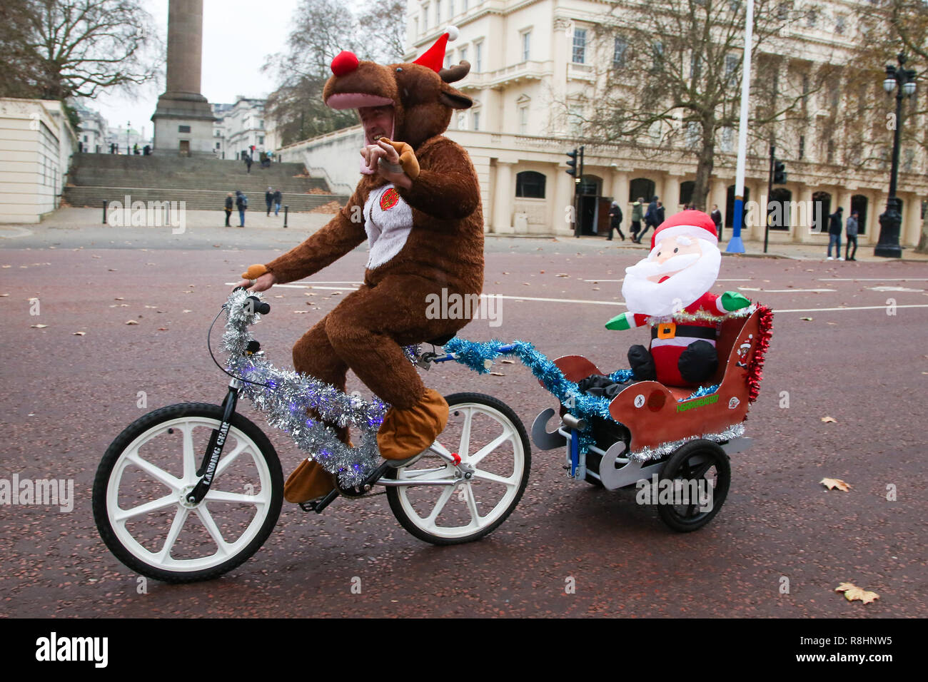 London, UK. 15th Dec, 2018. A man dressed as Father Christmas with an inflated Father Christmas is seen on The Mall as he cycles during the event.Cycling through London to raise awareness and money for Evelina London Children's Hospital (ECHO), for children with heart conditions. The annual event began four years ago after Stephane Wright's son Tommy, suffered a heart attack and spent time at Evelina London. Tommy was only 6 months old when he suffered a heart attack and nearly died. Fortunately Tommy recovered well but will require further operations as he grows up, so wil Stock Photo