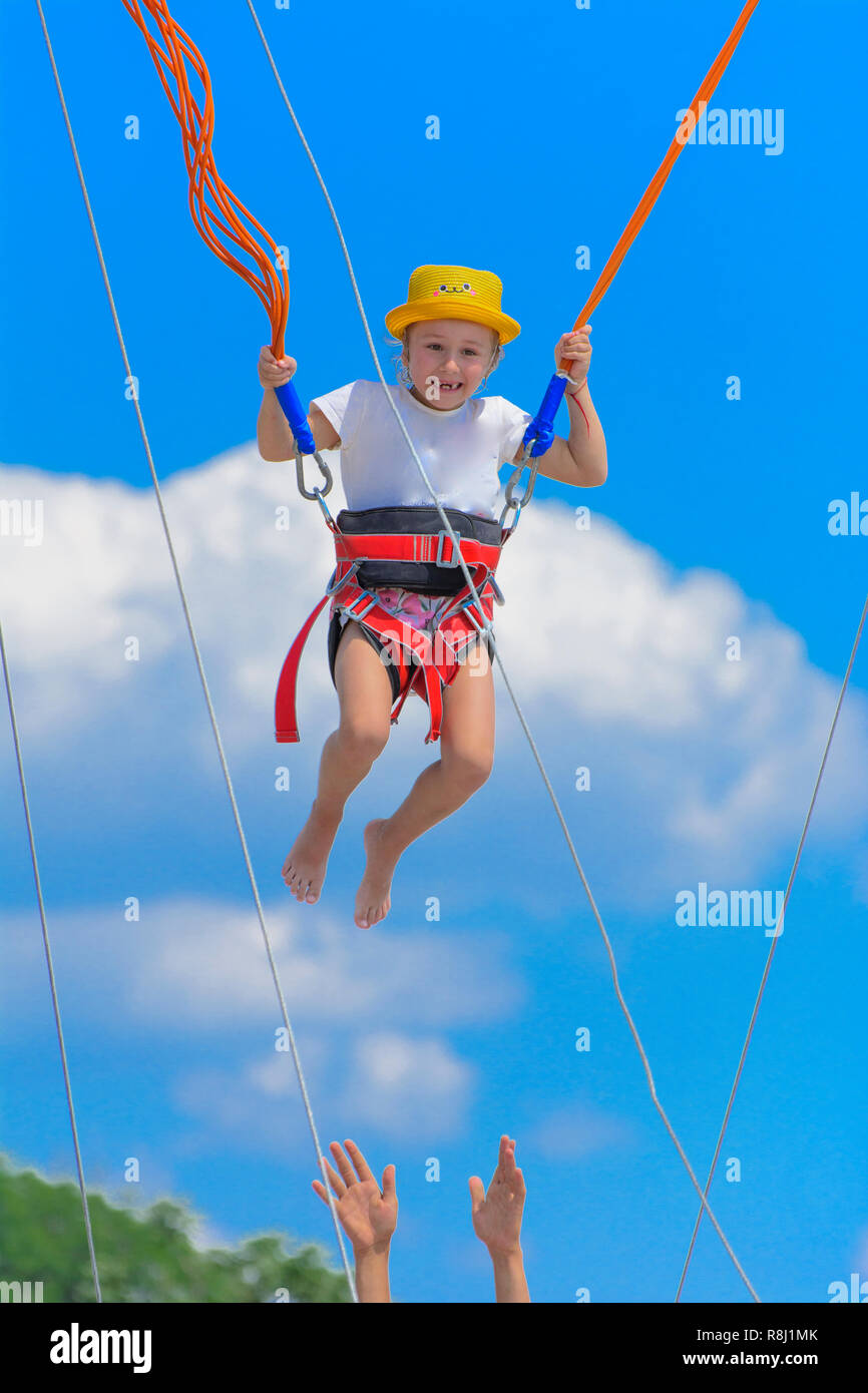 A little girl jumps high on a trampoline with rubber ropes against the blue  sky and white clouds. Adventures and extreme sports. Concept of summer vac  Stock Photo - Alamy