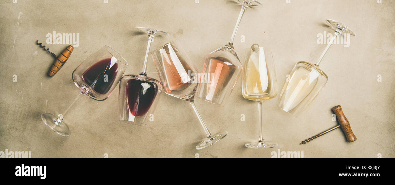 Flat-lay of red, rose and white wine in glasses and corkscrews over grey concrete background, top view, wide composition. Wine bar, winery, wine degus Stock Photo