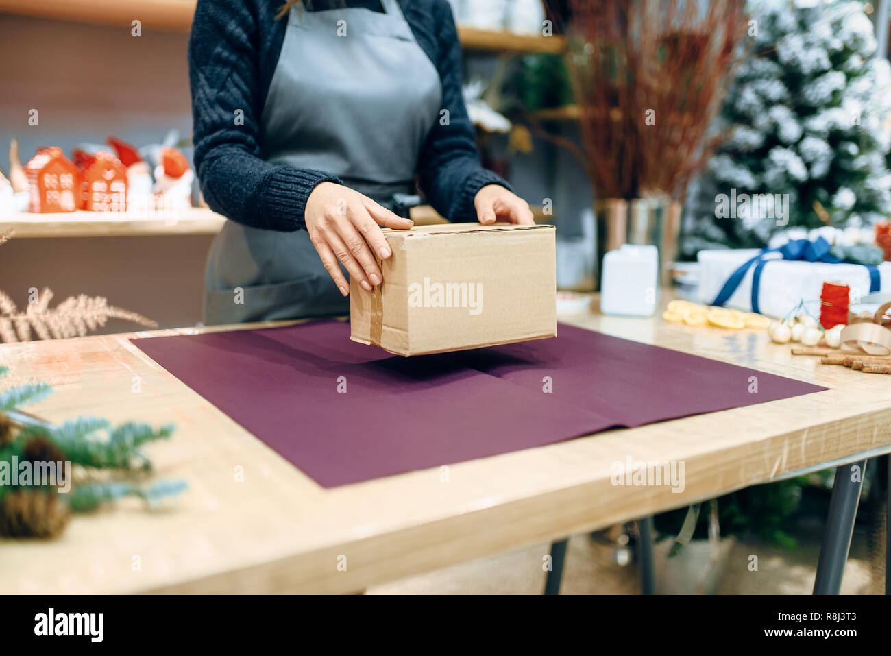 Female seller holds unwrapped carton gift box. Present wrapping papaer on the table, decoration procedure Stock Photo
