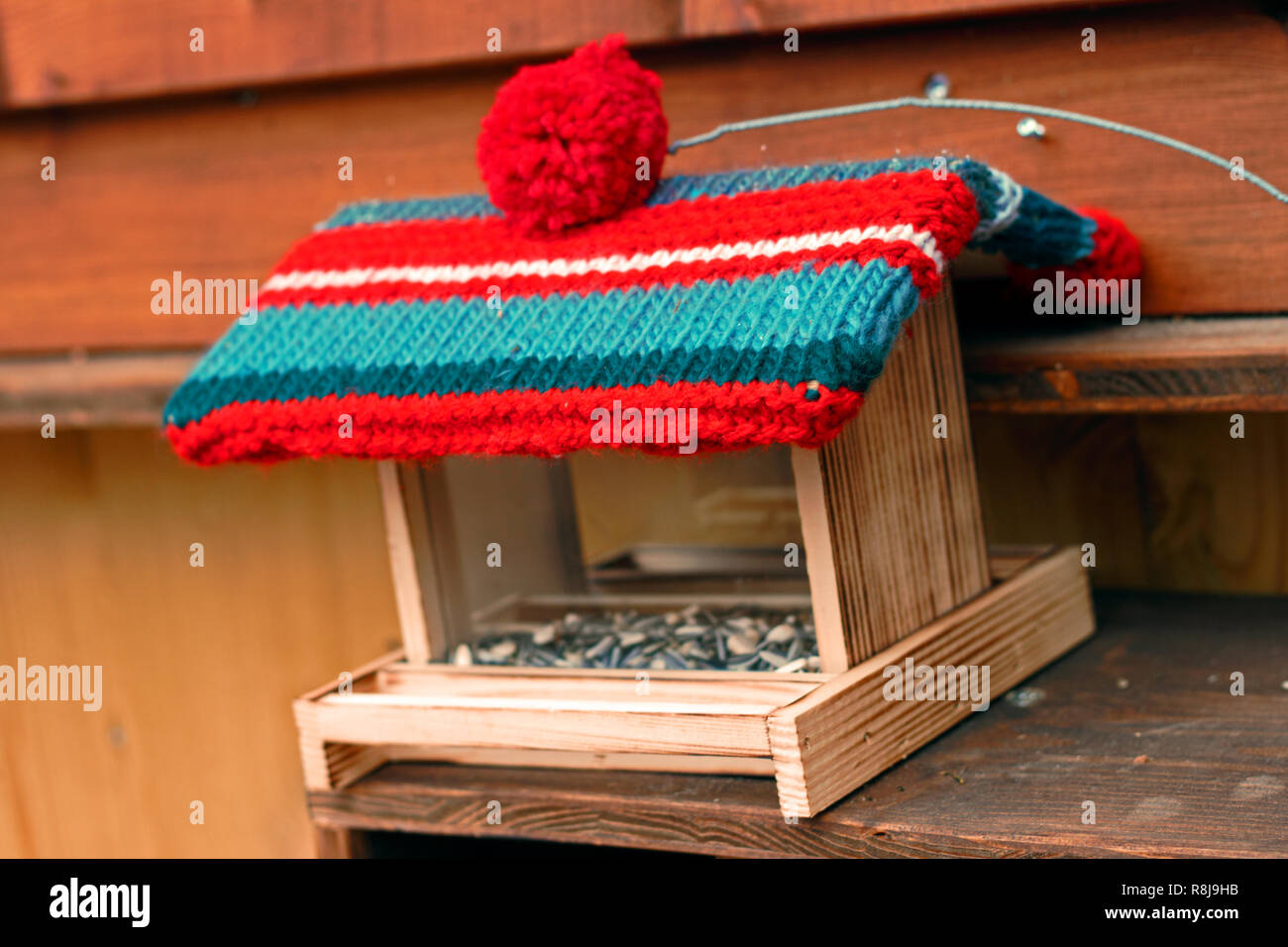 Wooden birdhouse carries a woolen jelly bag cap. Winter decoration. Stock Photo