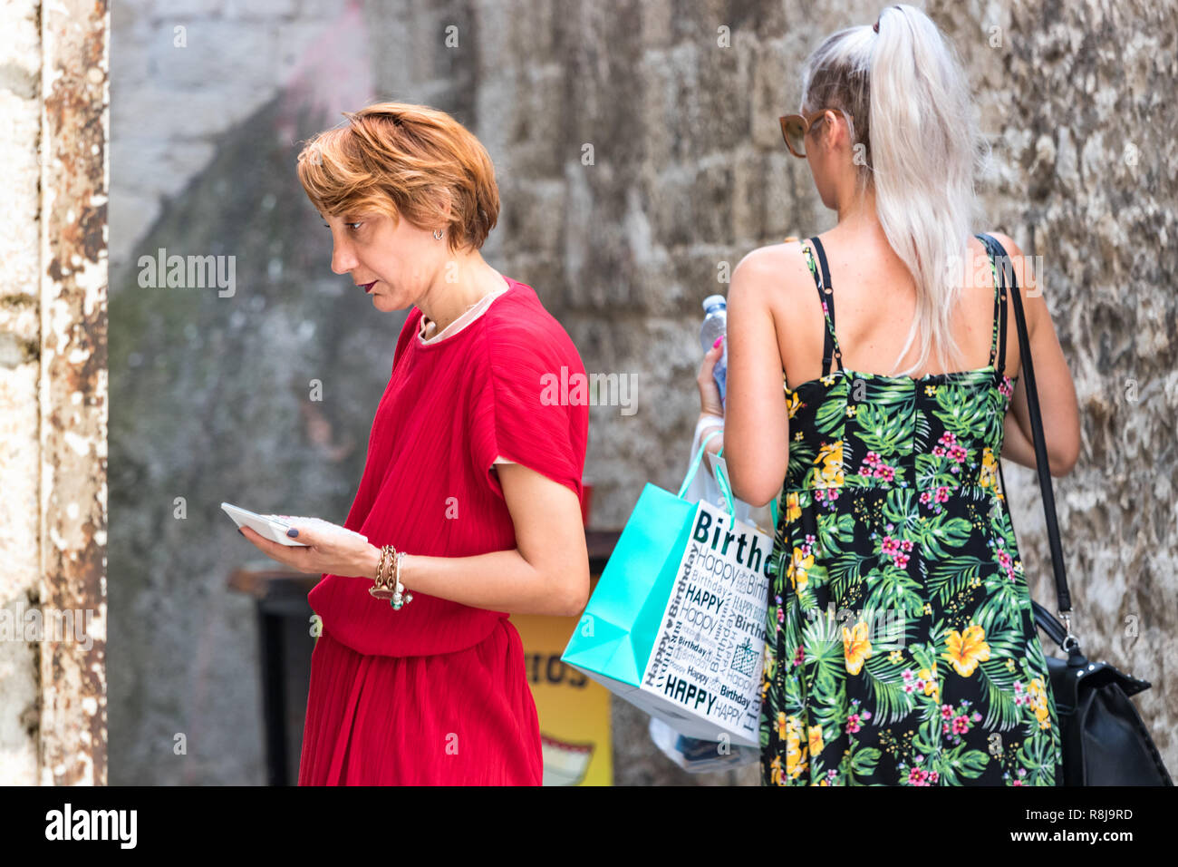 Croatia, Split - September 22th, 2018: A mature woman standing using a calculator outdoors checking the prices of her clothes store, Split, Croatia. Stock Photo