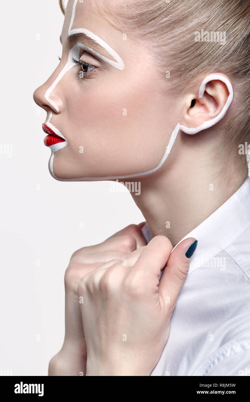 Side view of beautiful young woman on gray background. Female with an unusual creative makeup face painting. Girl with hands on collar Stock Photo