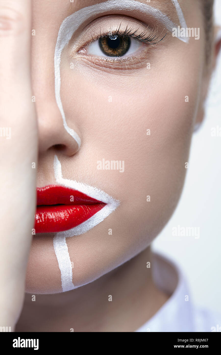 Beauty fashion portrait of a young woman on gray background. Female with an unusual creative makeup face painting. Girl with hands near face. Stock Photo