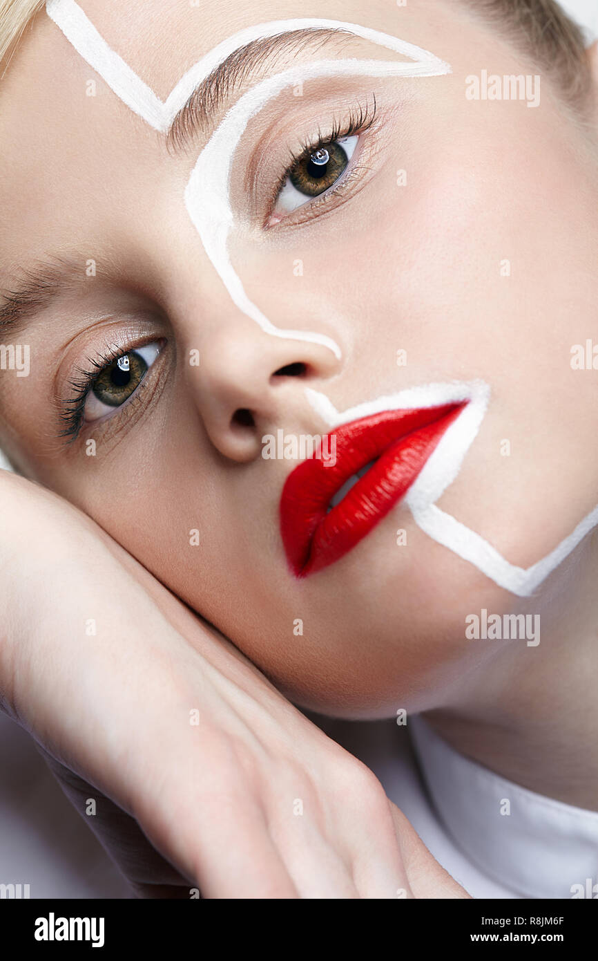 Beauty fashion portrait of a young woman on gray background. Female with an unusual creative makeup face painting. Girl with hands near face. Stock Photo