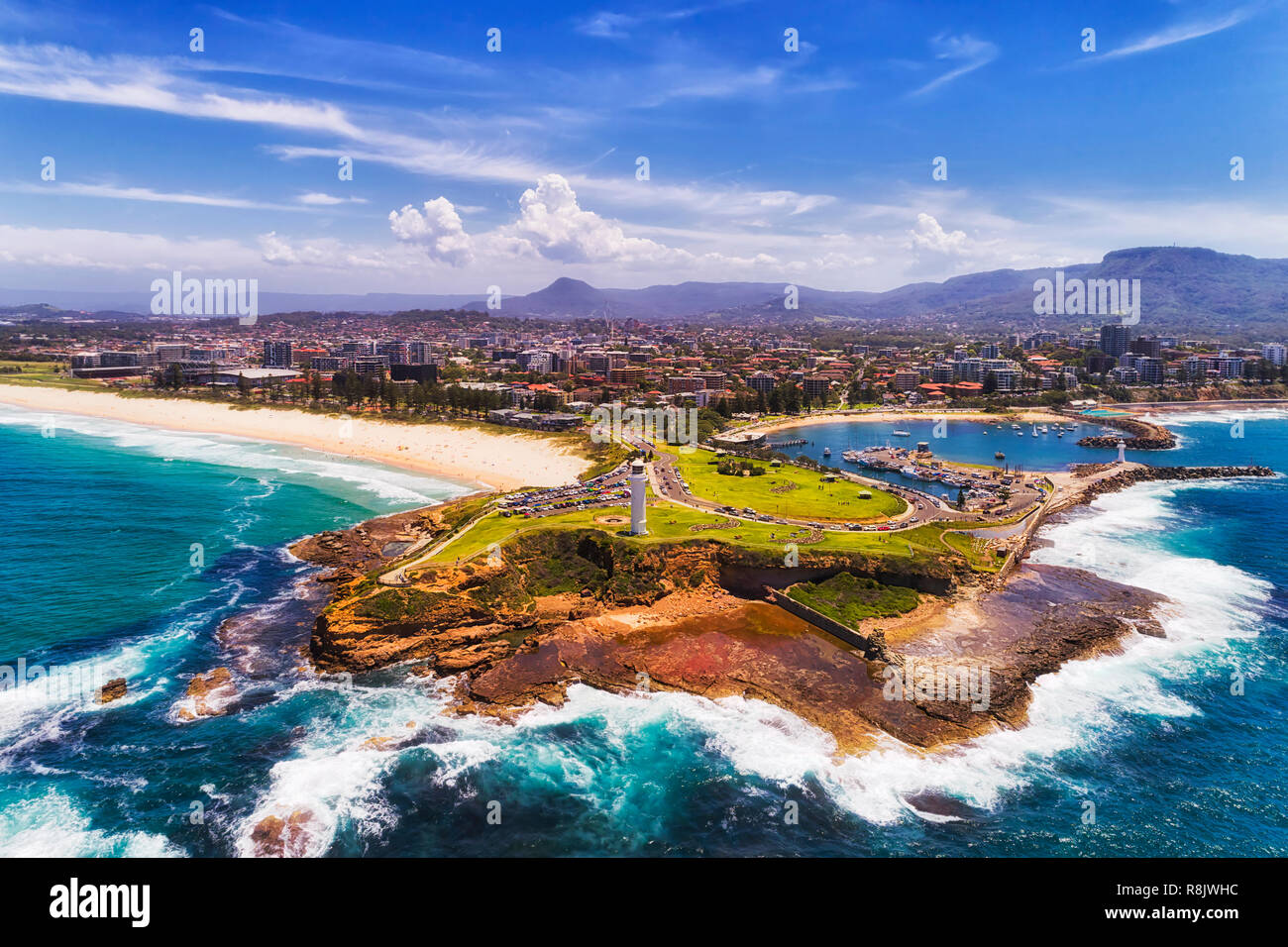 Headland of Wollongong city on Pacific coast of Australia with two white lighthouses guarding and protecting town harbour and marina in aerial view fr Stock Photo