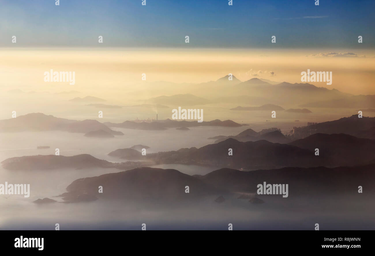 Elevated aerial view over achipelago of islands around Hong kong and Lantau covered by clouds and mist during sunset hour. Stock Photo