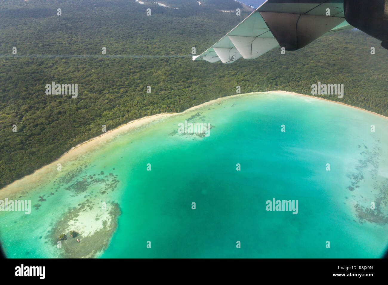 A view of azure lagoon and yellow sandy beach from a regional turboprop/propeller airplane window while arriving/departing Isle of Pines (L'Ile-des-Pins). Flying over New Caledonia, Melanesia, Oceania Stock Photo