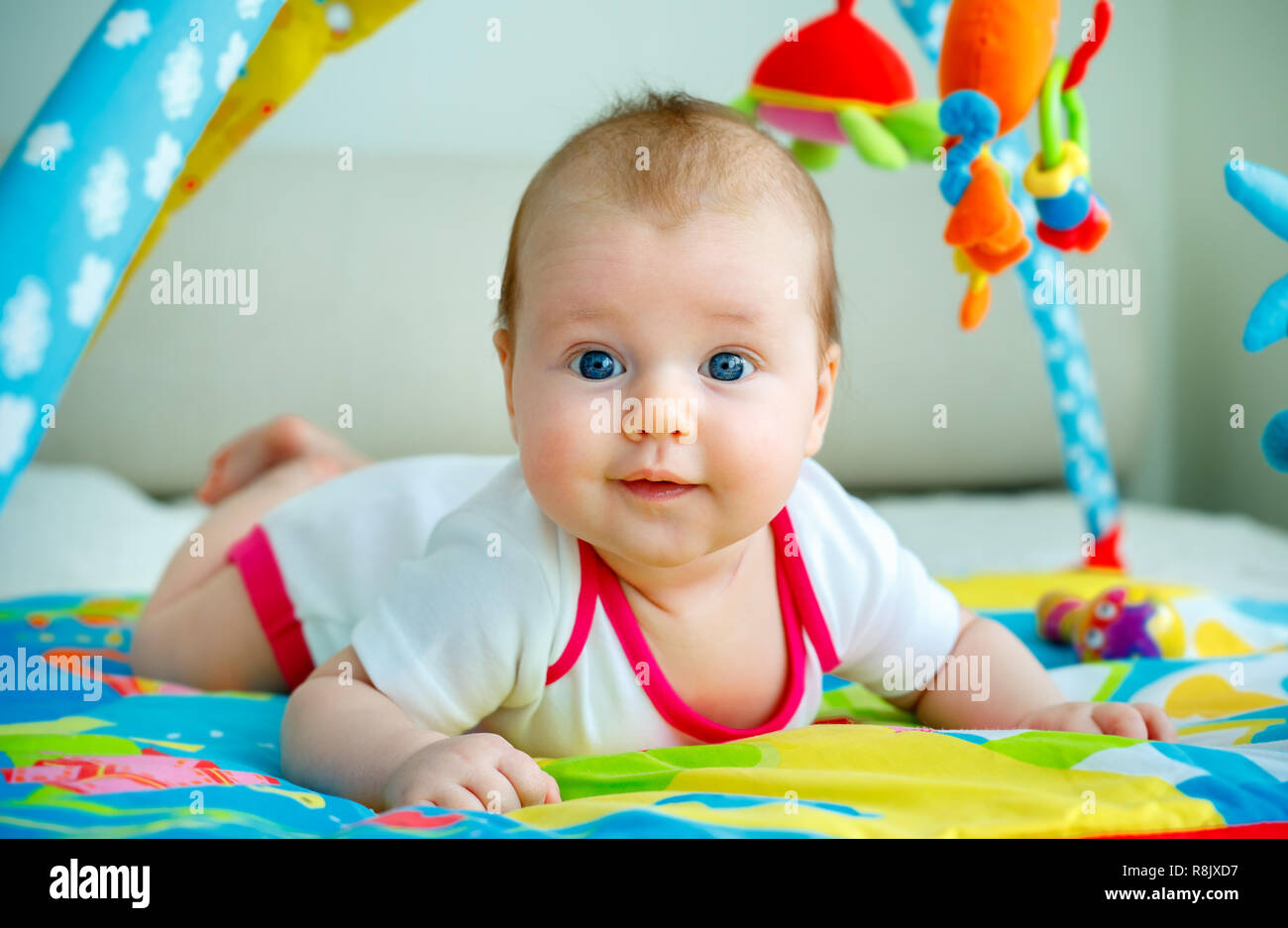 Adorable baby girl having fun with toys on colorful play mat Stock Photo